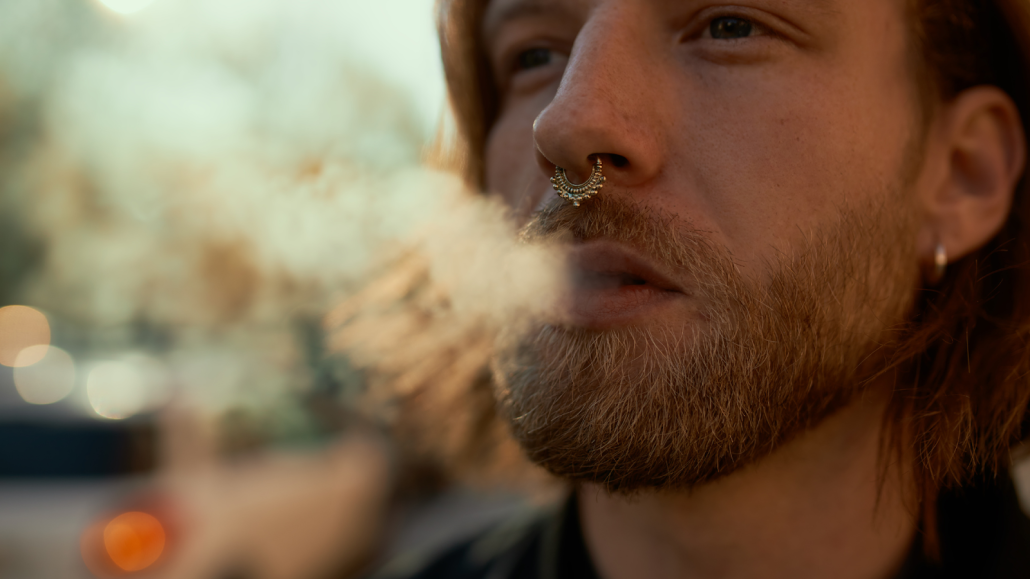 Man with spectum nose ring exhaling smoke.