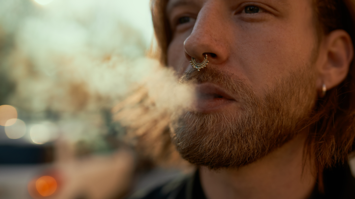 Man with spectum nose ring exhaling smoke.