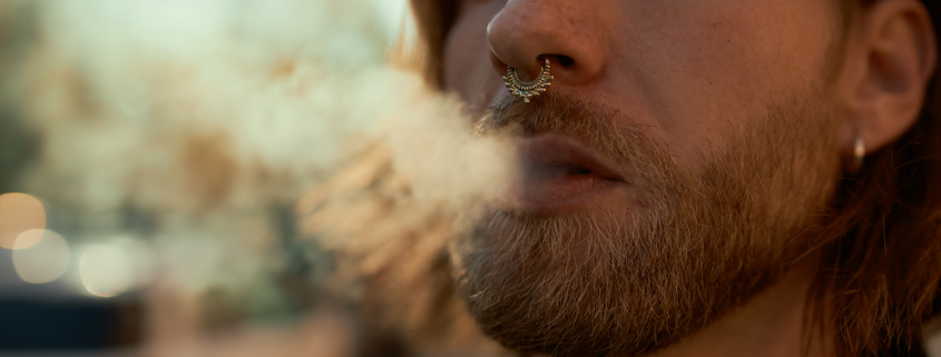 Man with spectum nose ring exhaling smoke.